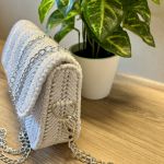 Torebka pleciona w jodełkę w kolorze białym z srebrnym akcentem - Prezentacja grubości torebki, detali splotu i zaczepienia łańcuszka.