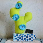 Kompozycja z kaktusem - niebieski - Kaktus uszyty z bawełny, ozdobiony ręcznie robionymi kwiatkami - tym razem niebieskie. Wypełniony miękką kulką silikonową. Deska drewniana pomalowana bezwonną farbą akrylową. Ozdobiona kropeczkami metodą decoupage.