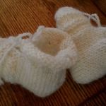 Buciki dla niemowlaka białe - buciki z włóczki białej niegryzącej, na zdjęciu widać zawiązywanie, wysokość cholewki, cholewka lekko wywinięta tworzy ciepły otulacz wokół kostek niemowalaczka