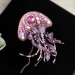 3D broszka Meduza, Ręcznie haftowana unikatowa biżuteria - Broszka ma solidne zapięcie ze stali nierdzewnej (typu agrafka) z obrotowym zabezpieczeniem, które zapobiega jej zgubieniu. Kolor srebrny. - Tył broszki wykonany jest z ciemnej zielonej skóry ekologicznej. - Kolorystyka - jasne odcienie różowego, purpurow