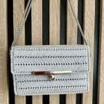 Makramowa torebka damska na ramię do eleganckich stylizacji - Biała torebka ze srebrną nitką w jodełkę, widoczna z przodu, z metalowym zamekiem i łańcuszkowym paskiem.